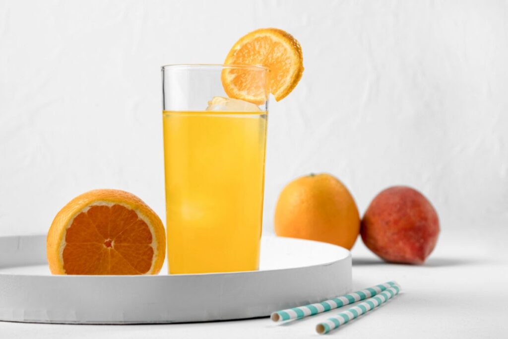 A refreshing glass of orange Vitamin Water garnished with a slice of orange, surrounded by whole fruits, showcasing the vibrant and nutritious beverage. Does Vitamin Water have caffeine?