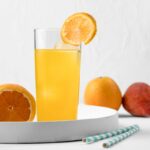 A refreshing glass of orange Vitamin Water garnished with a slice of orange, surrounded by whole fruits, showcasing the vibrant and nutritious beverage. Does Vitamin Water have caffeine?