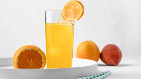 A refreshing glass of orange Vitamin Water garnished with a slice of orange, surrounded by whole fruits, showcasing the vibrant and nutritious beverage. Does Vitamin Water have caffeine?