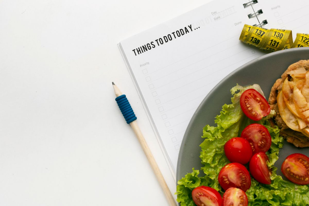 A healthy meal on a plate with a to-do list, pencil, and measuring tape on a white surface.