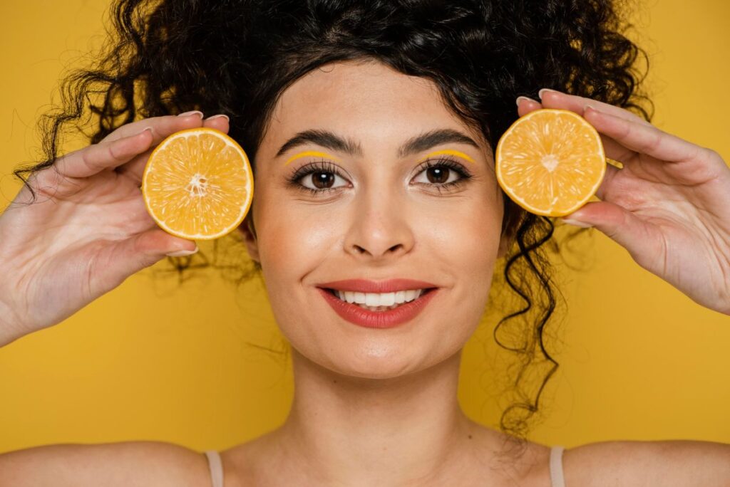 Woman holding orange slices to her face, representing Vitamin C Serum Before and After effects on skin.