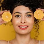 Woman Holding Orange Slices To Her Face, Representing Vitamin C Serum Before And After Effects On Skin.