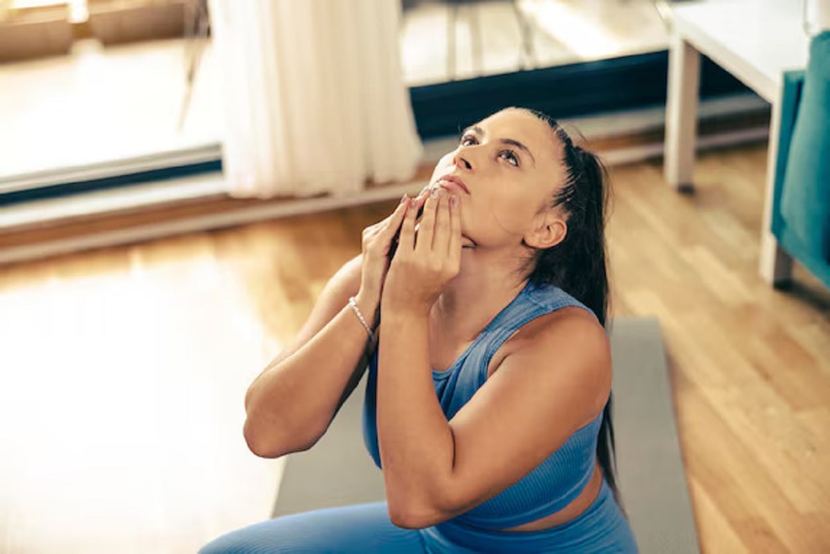 A woman in a blue workout outfit doing a chin lift exercise to lose neck fat