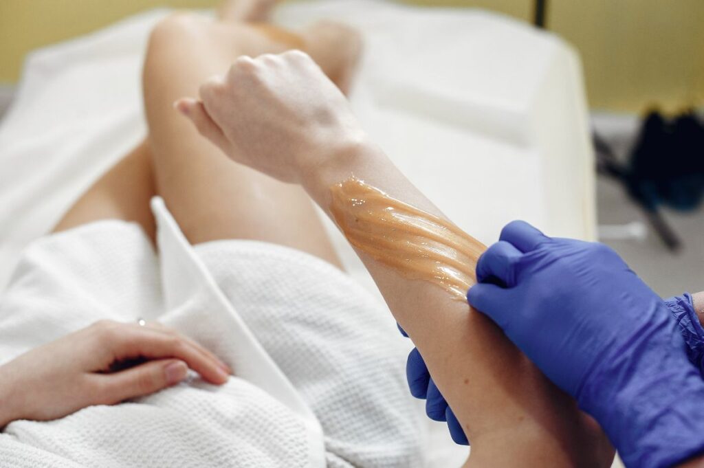 Person receiving a waxing treatment on their arm and revealing the truth Does Waxing Reduce Hair Growth?