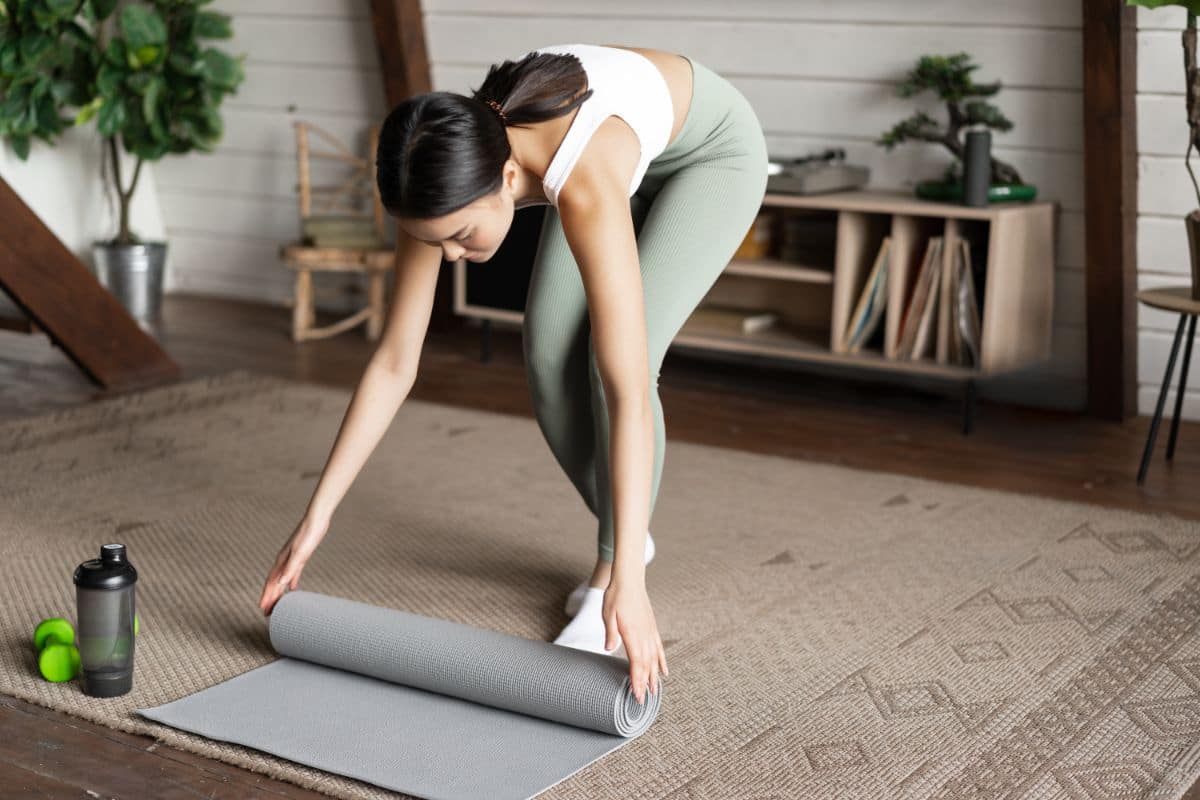 Woman in workout attire rolling out a yoga mat in a cozy living room.