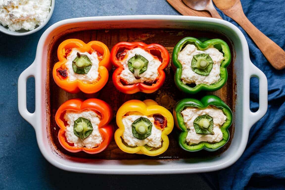 A baking dish containing colorful bell peppers (red, yellow, and green) stuffed with a savory mixture of cottage cheese and spinach, topped with the pepper tops.