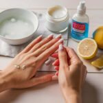 how to remove super glue from skin Hands with super glue on skin being treated with home remedies, including a bowl of warm soapy water, a jar of petroleum jelly, a bottle of acetone-based nail polish remover, and fresh lemon slices.