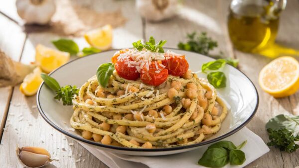 Chickpea Pasta A plate of spaghetti topped with roasted cherry tomatoes, chickpeas, and grated cheese, garnished with fresh basil, sitting on a rustic wooden table alongside lemon wedges, garlic, and olive oil.