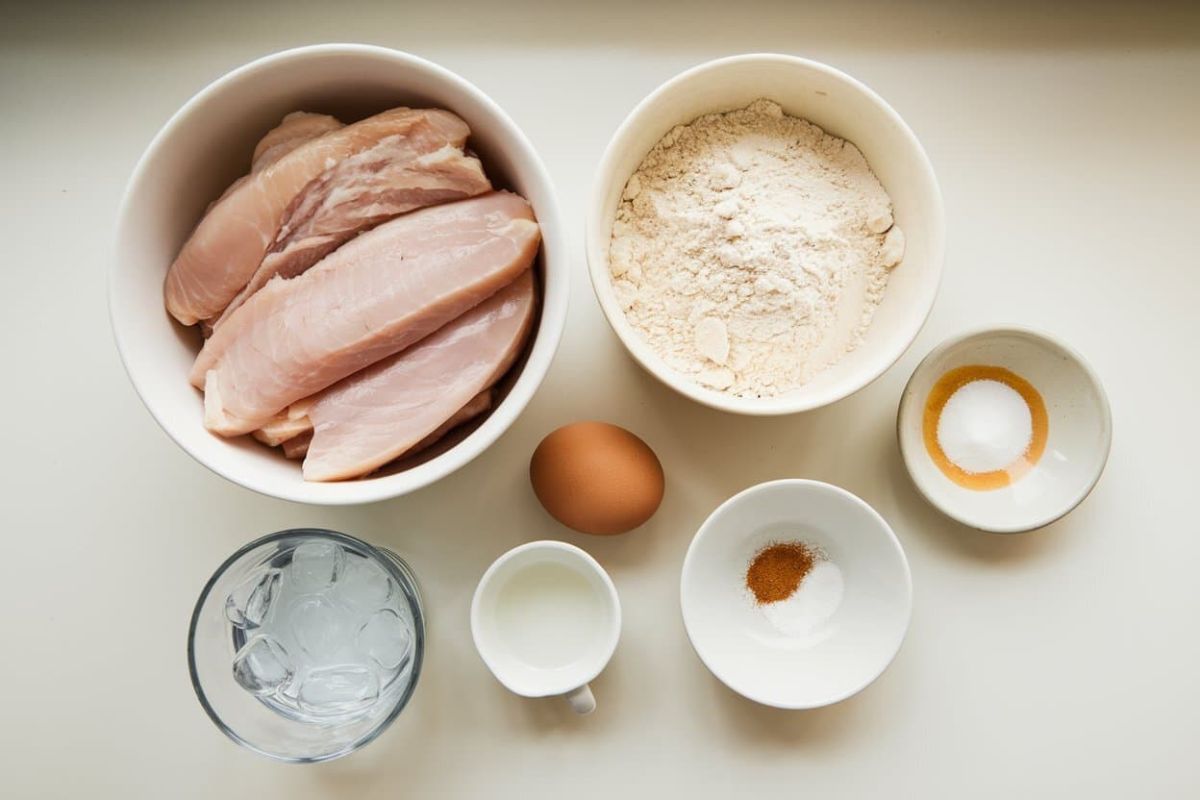 Ingredients For Making Chicken Tempura Laid Out On A Table, Including Raw Chicken Fillets, Flour, An Egg, Water With Ice, Milk, And Seasonings.