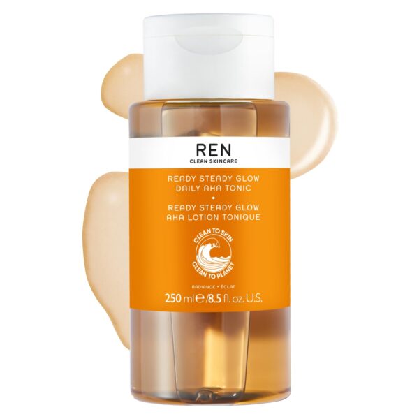 A Bottle Of Ren Clean Skincare Ready Steady Glow Daily Aha Tonic, 250Ml, With A Pump Dispenser And Orange Label, Surrounded By Two Beige Liquid Smears.