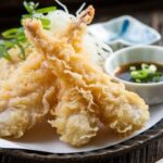 A plate of crispy chicken tempura served with a side of dipping sauce garnished with green onions.