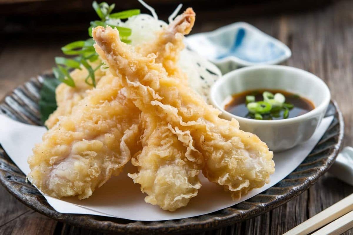 A plate of crispy chicken tempura served with a side of dipping sauce garnished with green onions.
