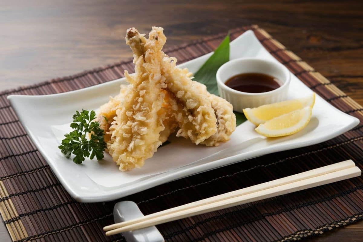Crispy chicken tempura served on a white rectangular plate with dipping sauce, lemon wedges, and a parsley garnish.