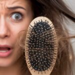 Woman looking shocked while holding a hairbrush with strands of hair, indicating hair loss problem.