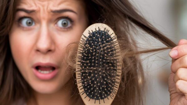 Woman looking shocked while holding a hairbrush with strands of hair, indicating hair loss problem.