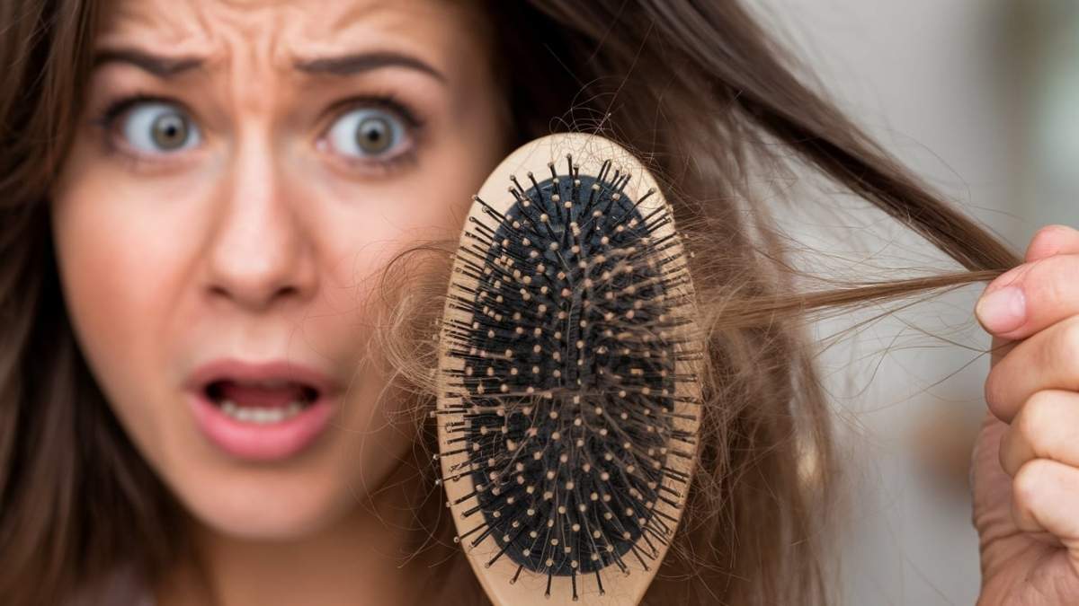 Woman looking shocked while holding a hairbrush with strands of hair, indicating hair loss problem.