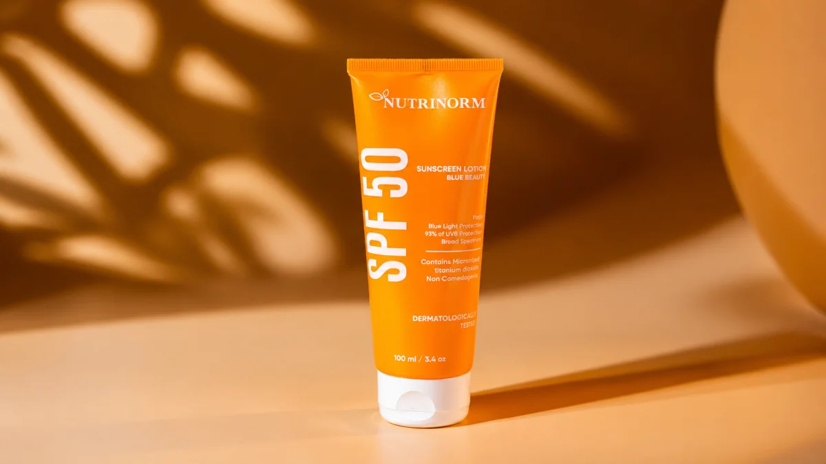 Nutrinorm Spf 50 Sunscreen Lotion Blue Beauty Tube Standing Upright On A Warm Beige Surface With Tropical Leaf Shadows In The Background, An Essential Sunscreen Step In A Daily Body Care Routine.