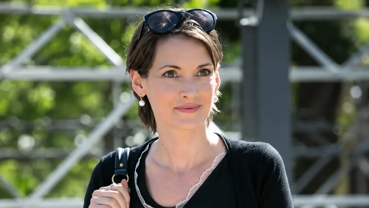 Winona Ryder Inspires the Rise of the Textured French Pixie Cut 2 Winona Ryder Posing Outdoors In A Black Outfit With Sunglasses On Her Head, Captured With Natural Lighting.