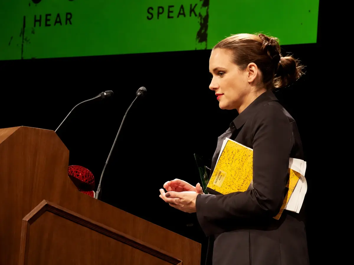 Winona Ryder Inspires the Rise of the Textured French Pixie Cut 3 Winona Ryder Standing At A Podium During A Public Speaking Event, Holding Papers And Speaking Under Stage Lights.